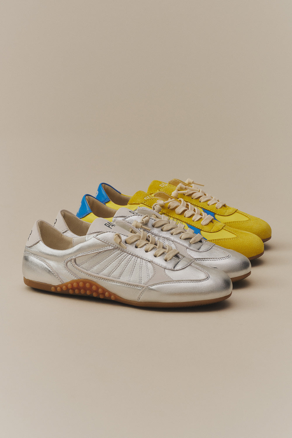 A stylish lineup of P448 sneakers featuring a slim, retro-inspired silhouette. The collection highlights a bold metallic silver finish and vibrant yellow suede with blue accents, accented by cream-colored laces and signature textured rubber soles.